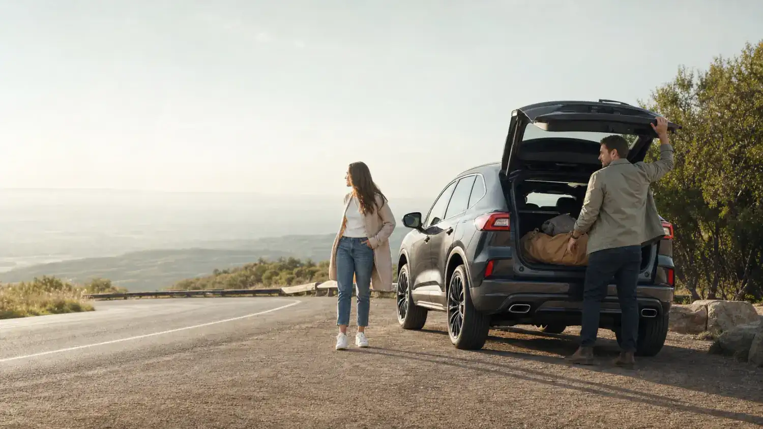 A couple loading bags into the back of an SUV at a roadside overlook